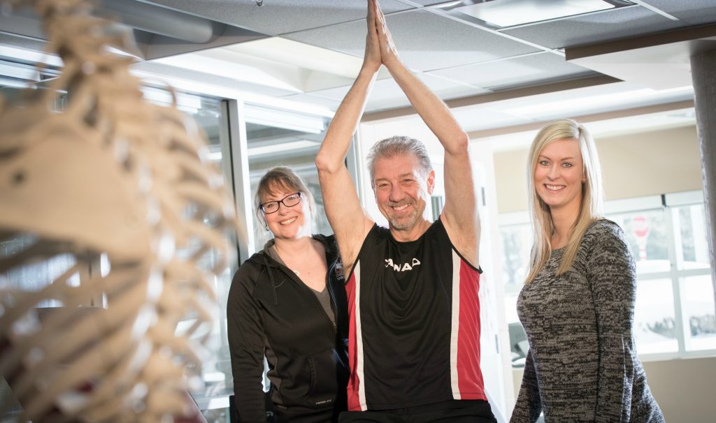 Steve Kalotinis proudly holds his arms above his head at the David Braley sport medicine clinic. Kalotinis worked closely with therapists at the clinic Sue Robinson, left, and Jillian Goodwin after having surgery on his shoulder.
