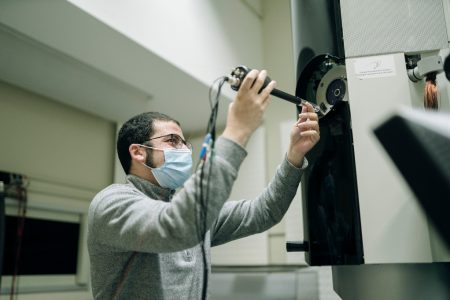 A man holding a long instrument works on an electron microscope 