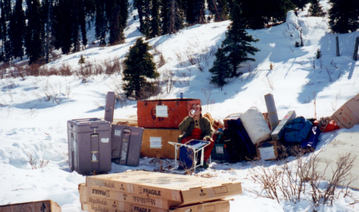 Man sitting in the snow surrounded by equipment.