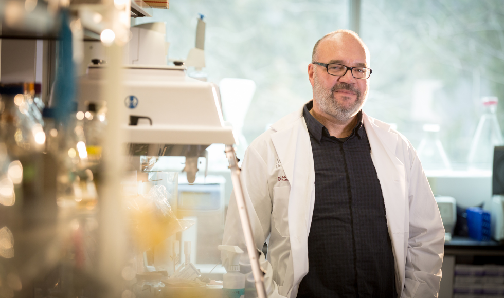 Gerry Wright wearing a white lab coat and standing inside a labratory