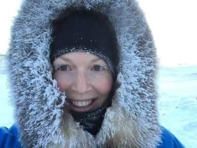 Gita Ljubicic standing out in the snow, smiling at the camera while bundled in winter clothing. 