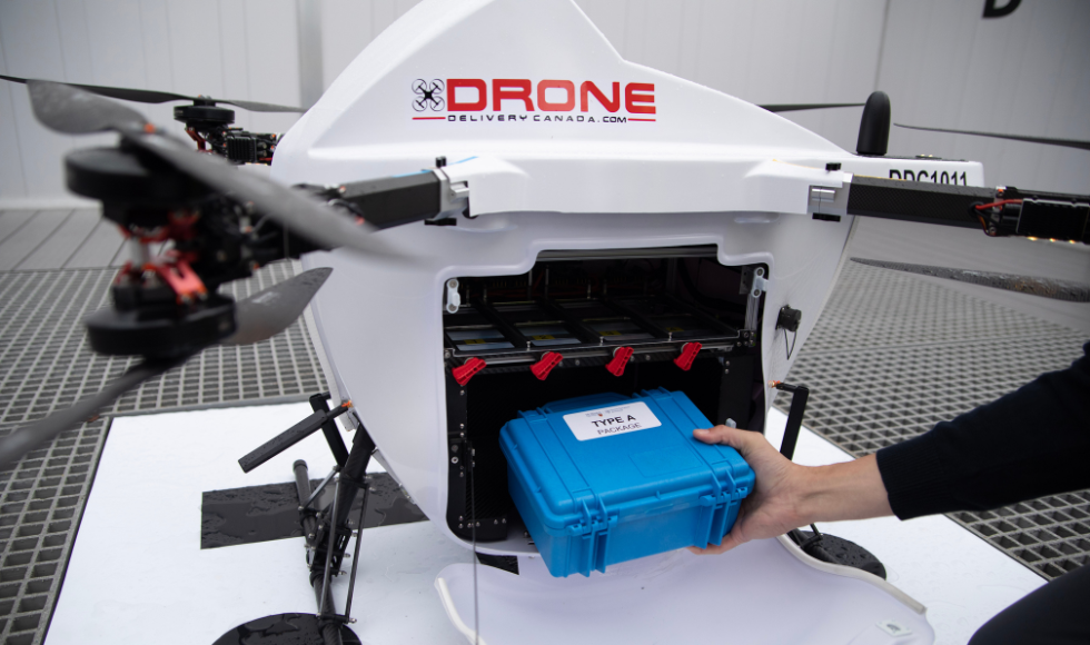 A hand holding a blue plastic container as it is loaded into a drone.