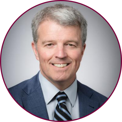 circular headshot of Greig Mordue, wearing a suit and tie