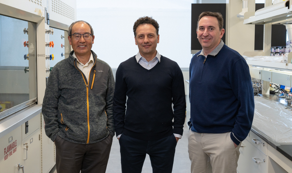 Three researchers standing side by side in a lab with their hands in their pockets, smiling at the camera