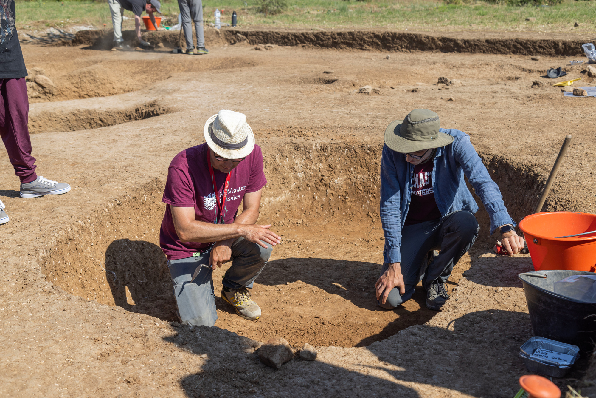 McMaster researcher Spencer Pope and a graduate student crouch down in an open pit to examine the dirt.