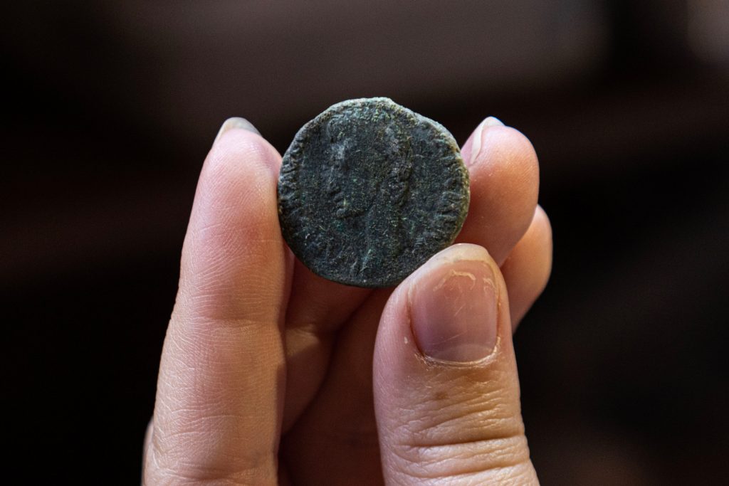 McMaster student Bronwyn Hathaway holds a coin she found during a dig at the Villa di Tito site. The coin is dark and covered in soot, but a face can be clearly seen.