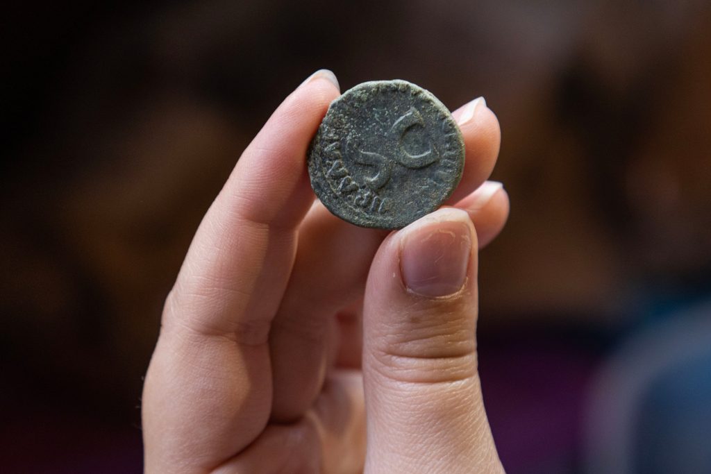 A student holds the backside of a Roman coin they dug up at Villa di Tito. It bears the initials S.C. on the back.