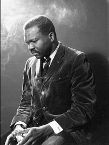 A black and white portrait of Austin Clarke as a young man, in a suit and tie.