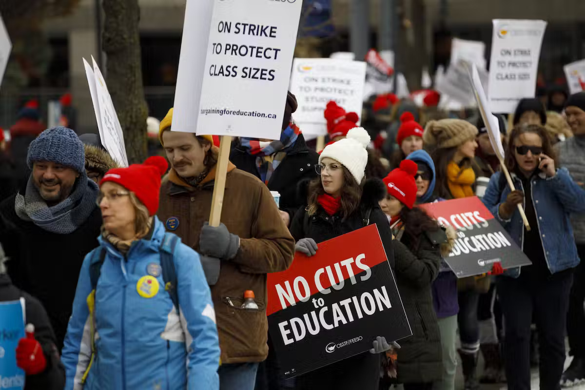 People holding protest signs that read, 'no cuts to education'