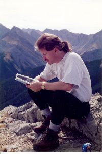 Daniel Coleman on top of a mountain reading a book 