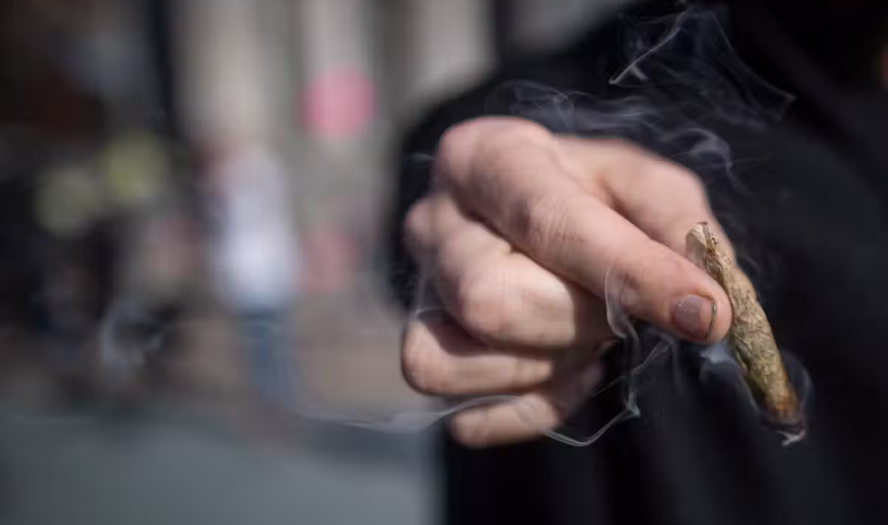 A hand holding a smoking cannabis joint 