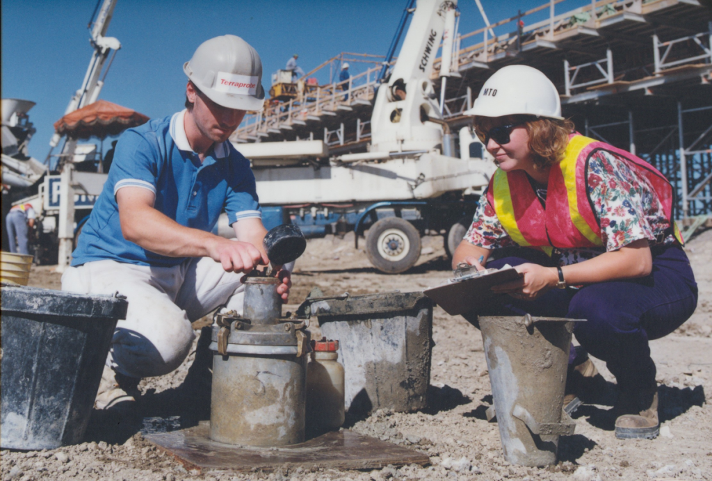 Two people in hard hats crouching down and working with concrete at a construction site.