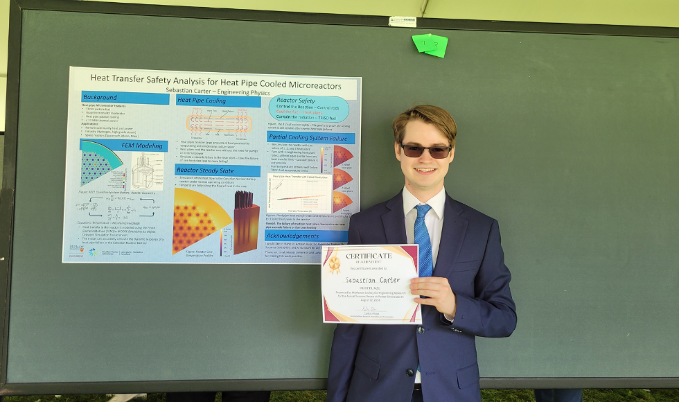 A person wearing sunglasses holding a certificate in their hands. Behind them is a research poster.