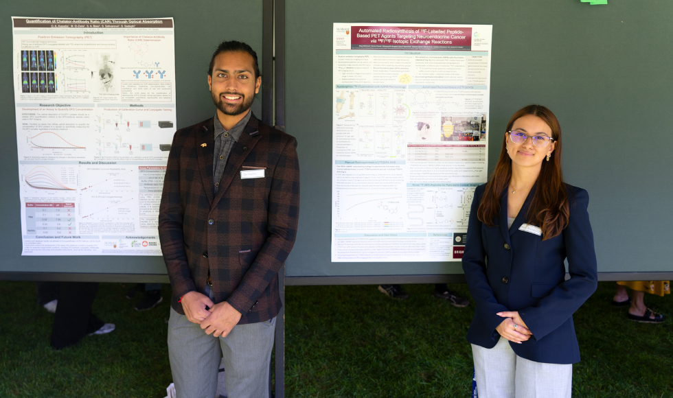 Two people standing smiling at the camera. Behind each of them is a research poster.