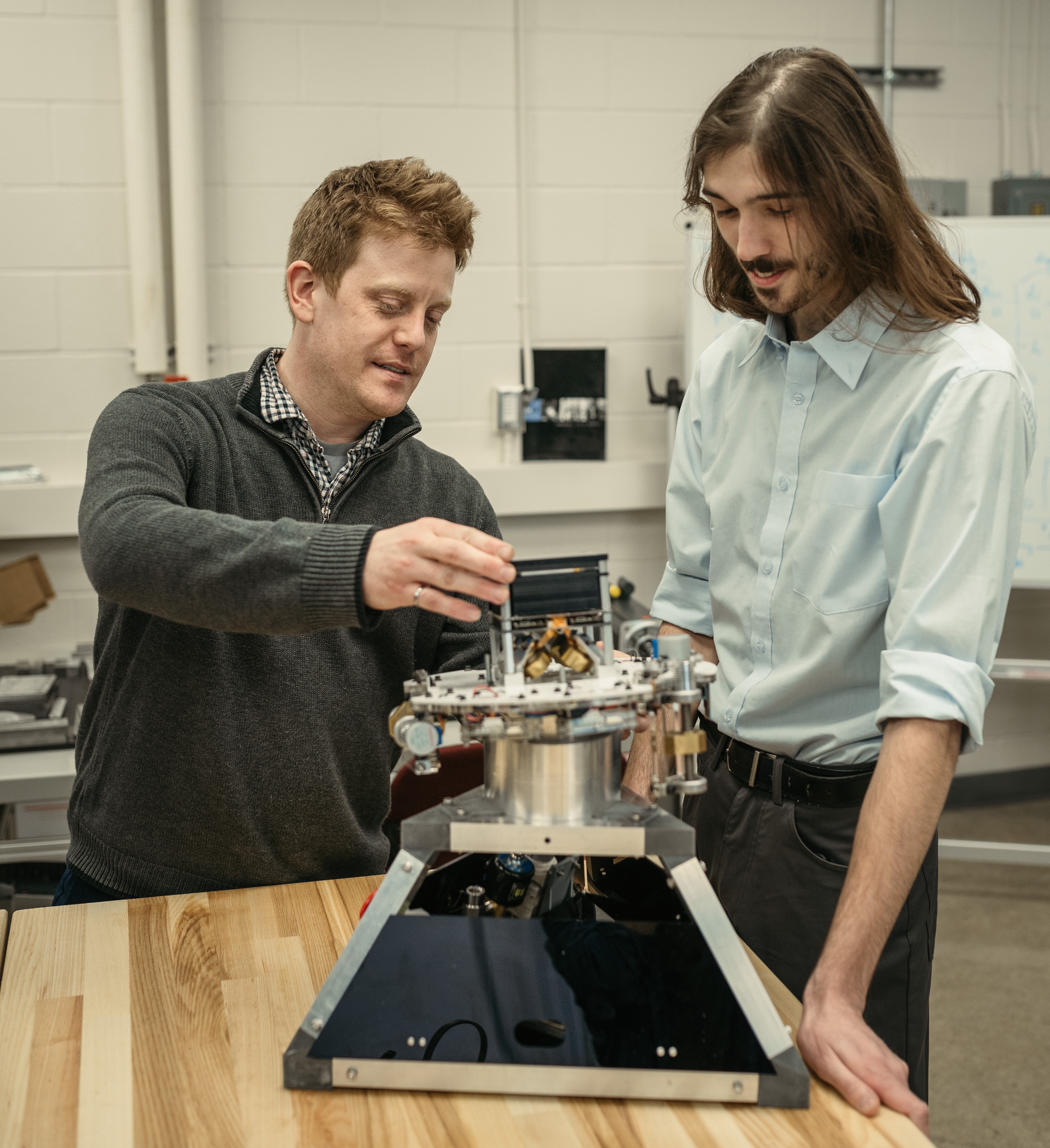 Two people work on a device on a tabletop indoors.