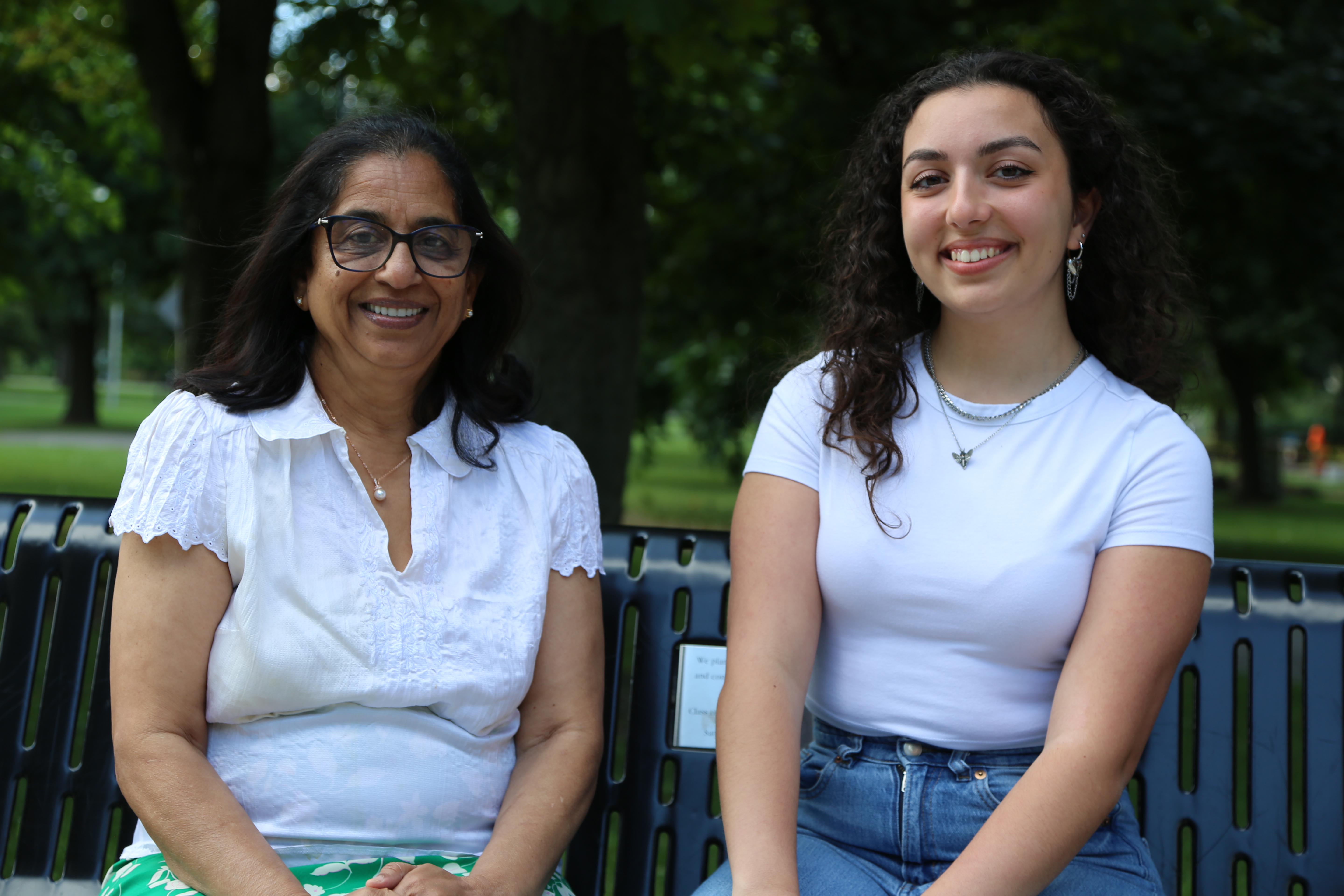 Two smiling women sit beside each other on a bench on McMaster's campus.