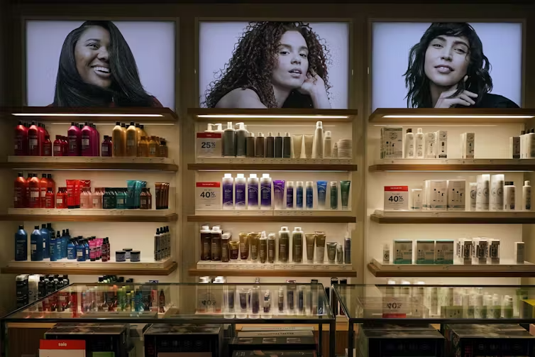 A shelf of cosmetics in a store, with photos of models above the shelving.
