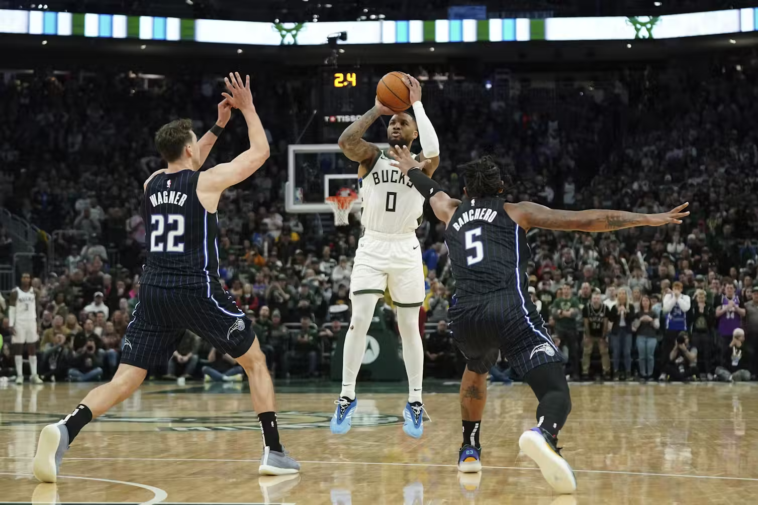 Three professional male basketball players during a game, with one player jumping to take a shot and two players from the opposing team trying to block him.