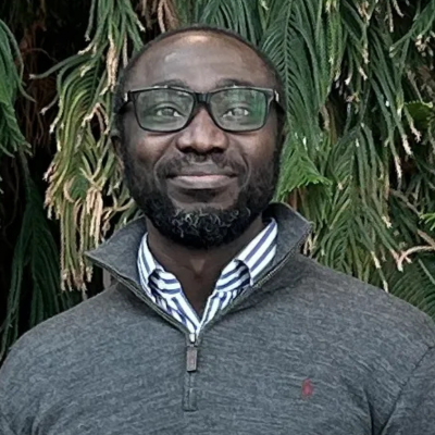 headshot of Joseph Okeme standing against a backdrop of greenery