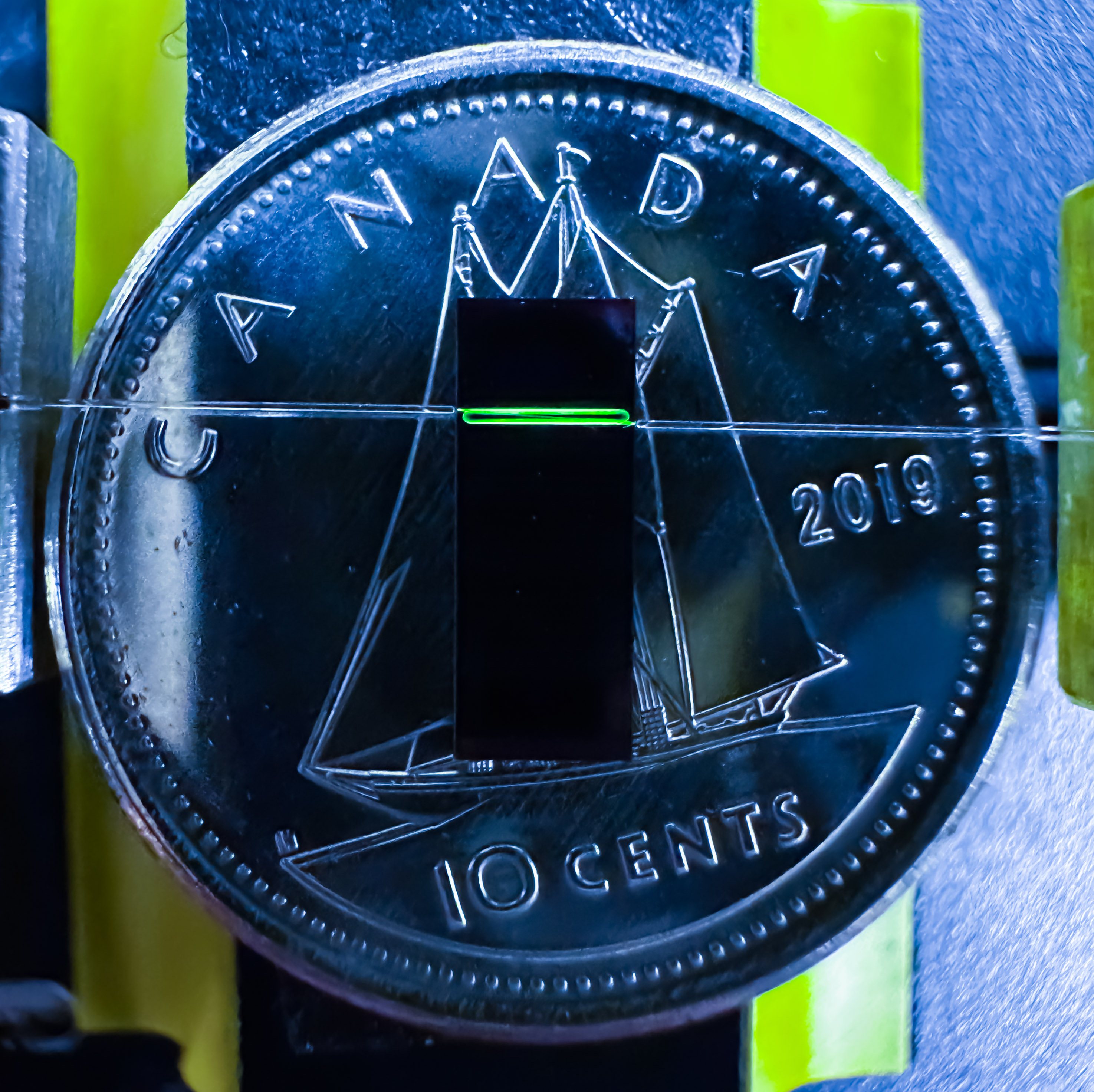 A Canadian dime with a small green line on it, and two more green lines behind the dime.