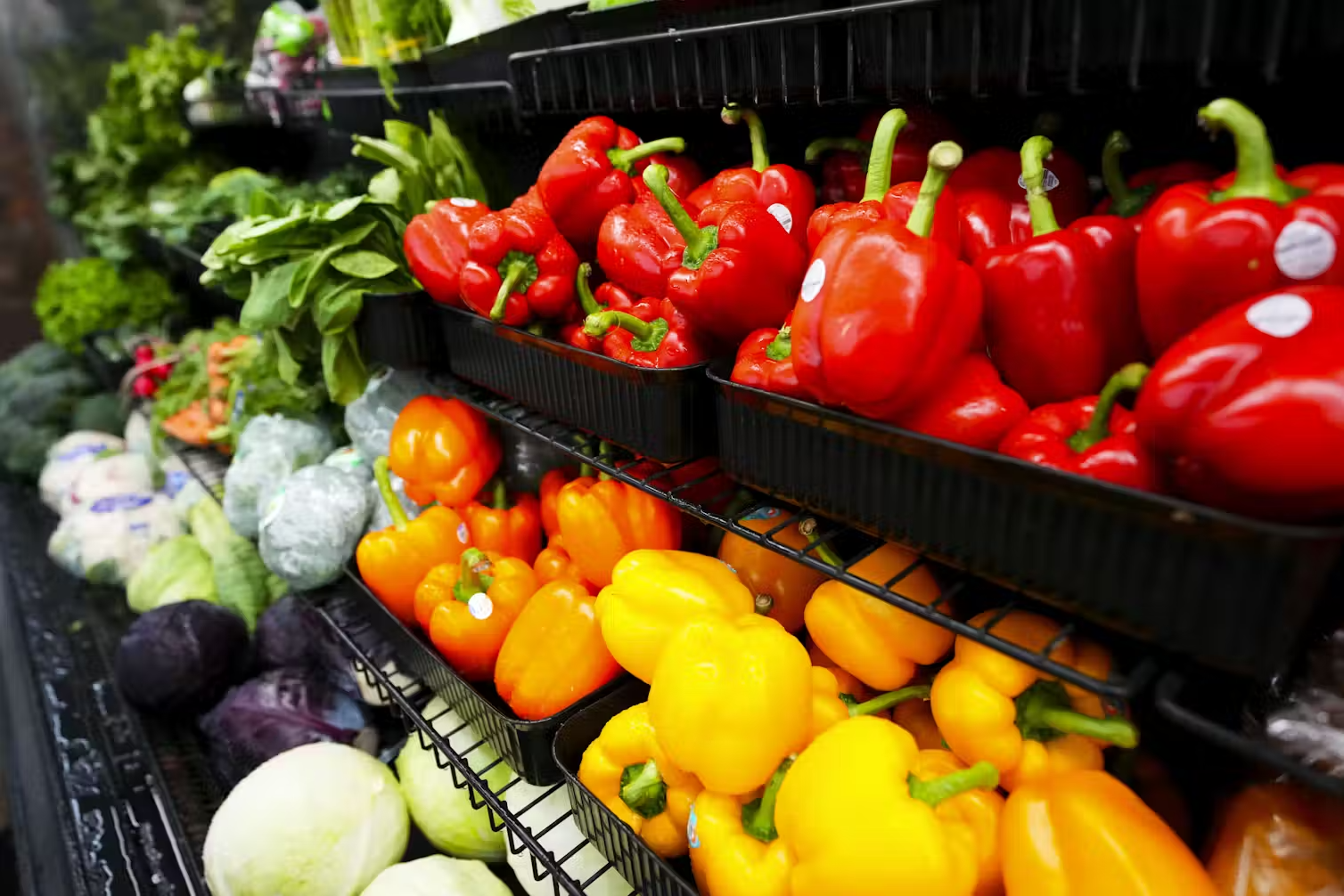 A larger shelf of fresh vegetables, including bell peppers and leafy greens.