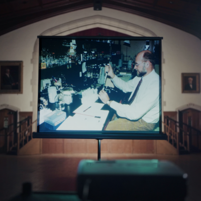 A projector screen showing an image of a scientist in a lab. 