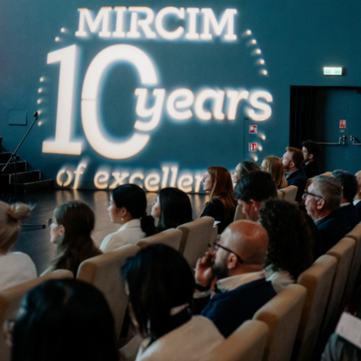 People sitting in theatre seats at a conference. On the wall the words "MIRCIM 10 years" are projected.
