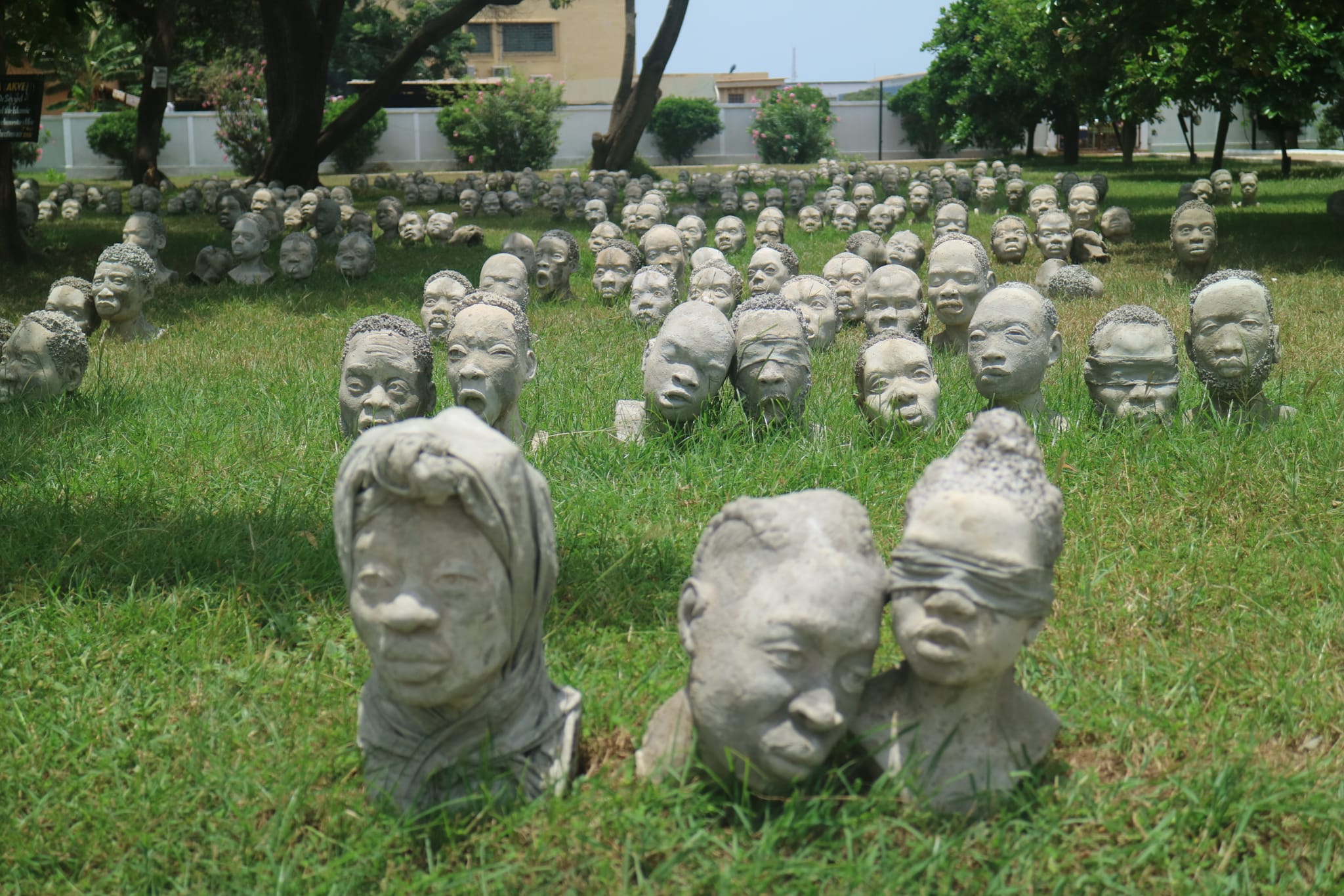 Dozens of stone heads, with facial expressions, sit on a grassy lawn.