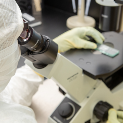 Over the shoulder look at a person in full head-to-toe protective lab gear looking into a microscope