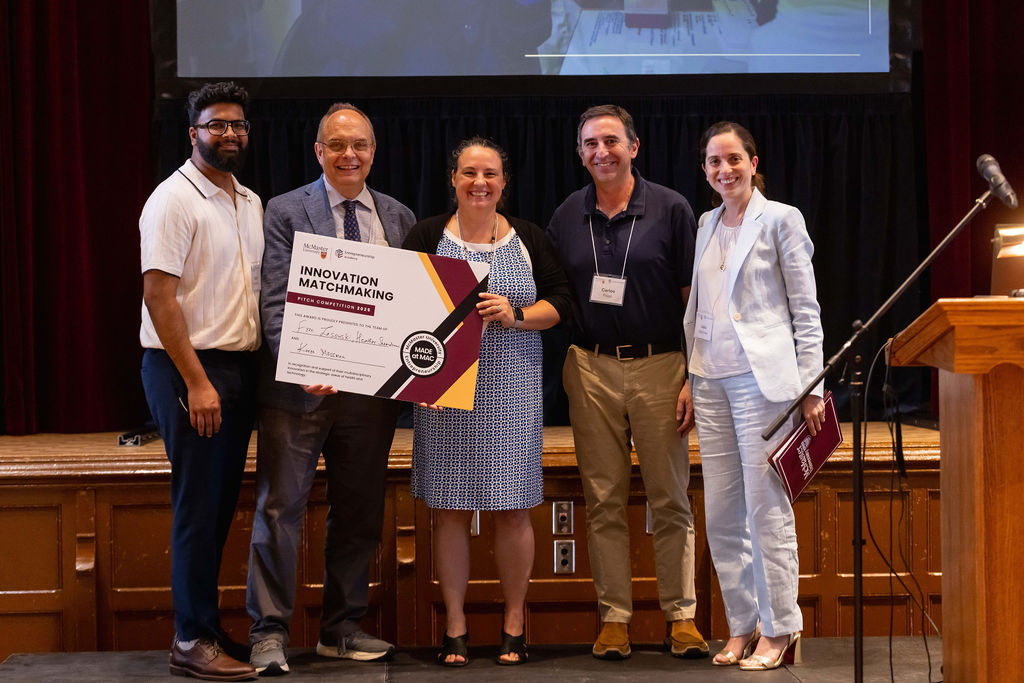 Five people stand together on stage holding a winner's plaque and smiling.