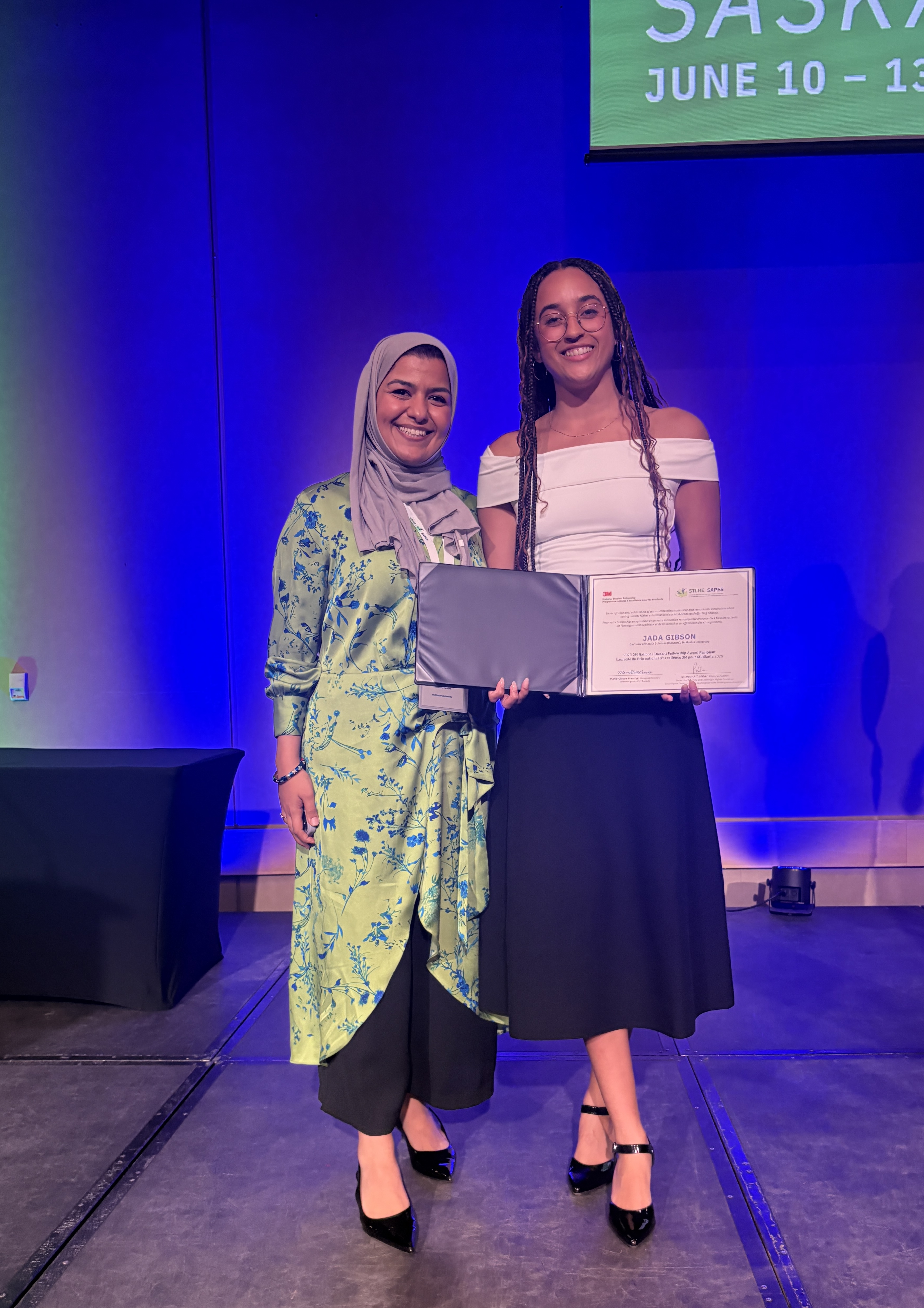 Two women stand on a stage, with one holding a certificate up.