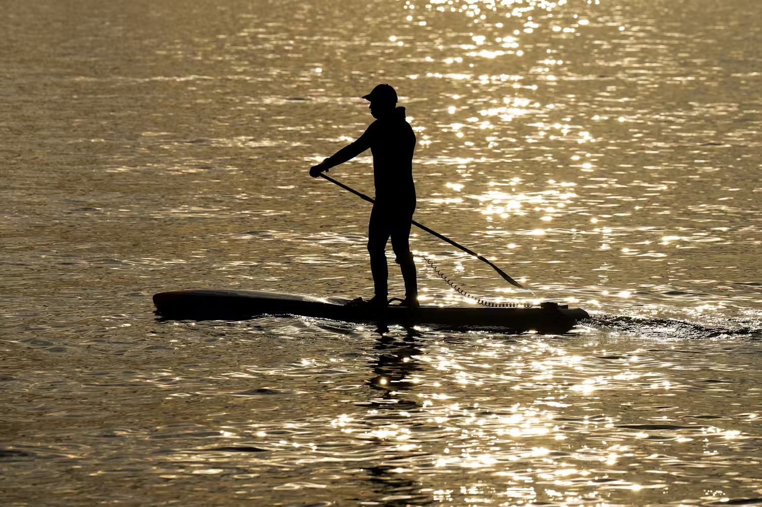 A person stand-up paddleboards on the water in golden light.