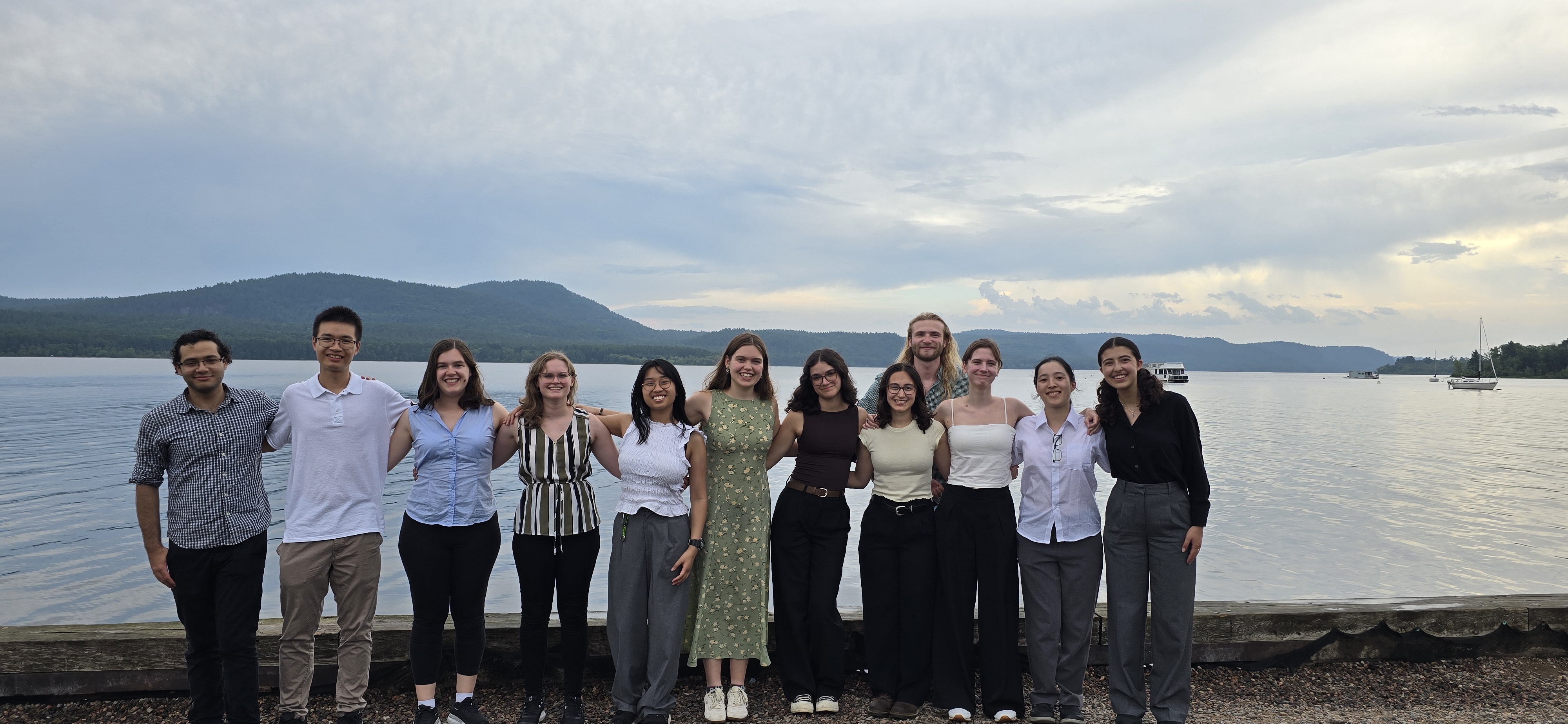 A group shot of twelve people standing beside a river.