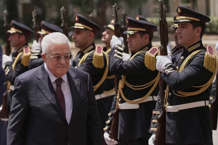 A man in a suit walks along a row of soldiers in dress uniforms.