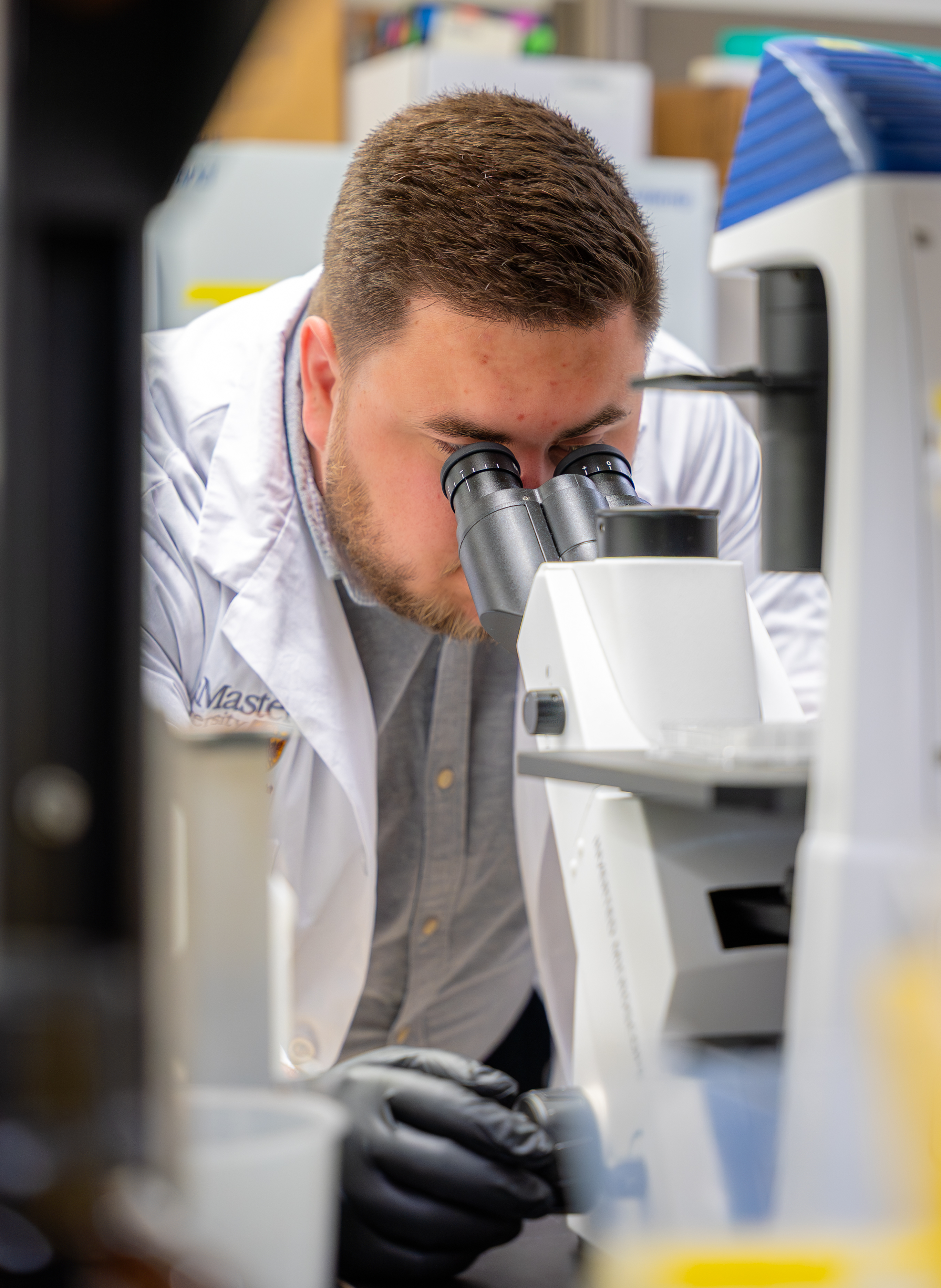 A man in a lab coat looks into a microscope.