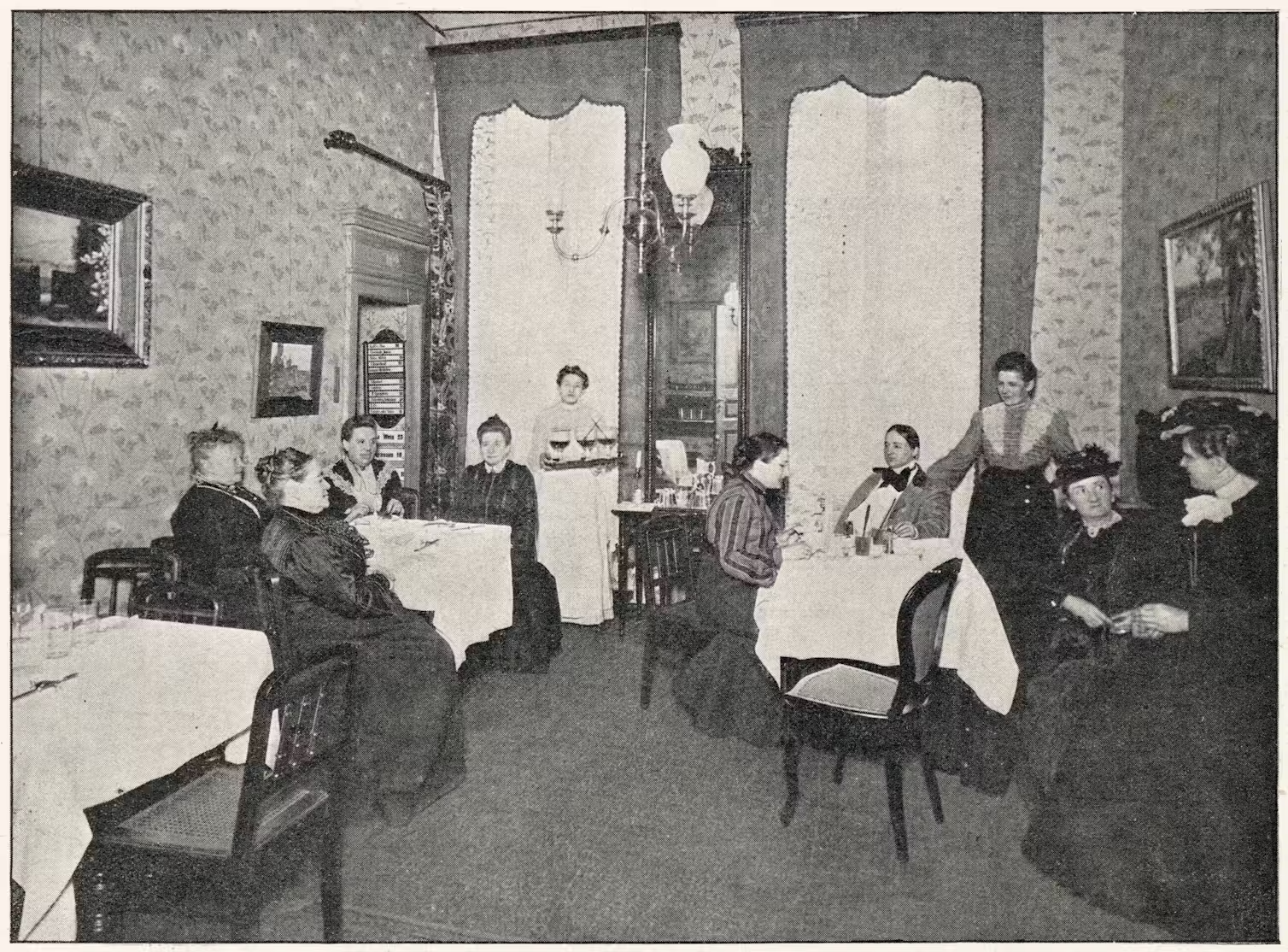 A black and white photo of people sitting at tables.