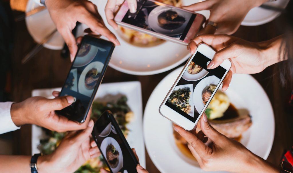 Many hands holding smartphones to take pictures of plates of food