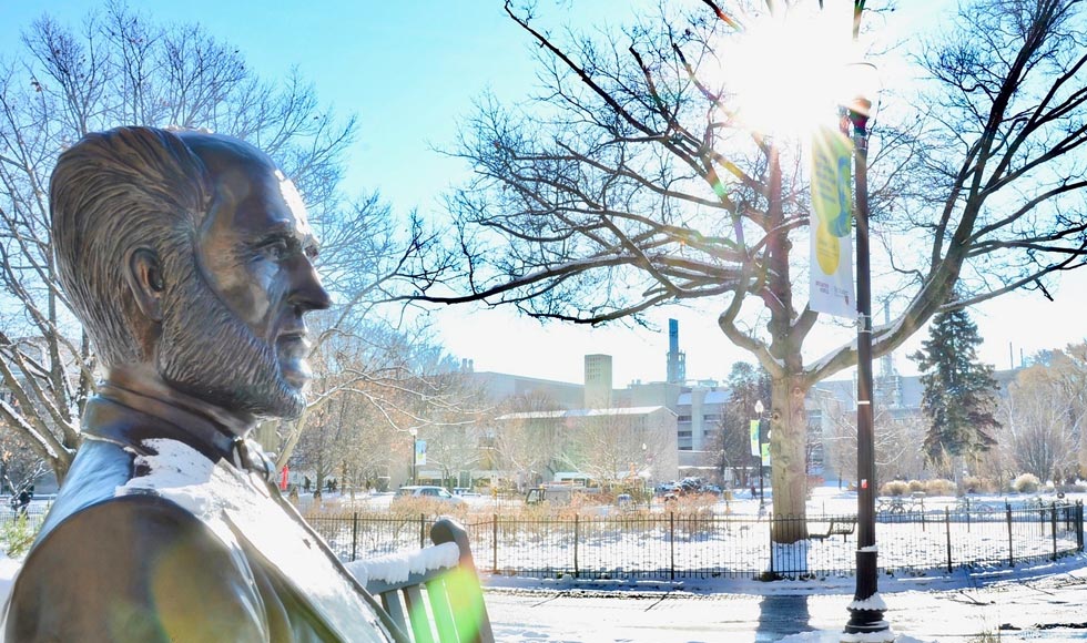Sun shining through the bare trees on Senator McMaster's statue in the winter.