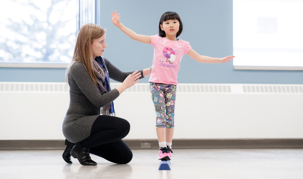 A child walks on a low balance beam assisted by a researcher
