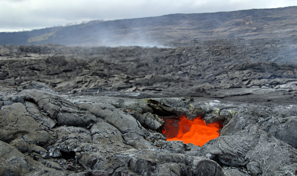 A grey rocky landscape with bright red lava in the middle