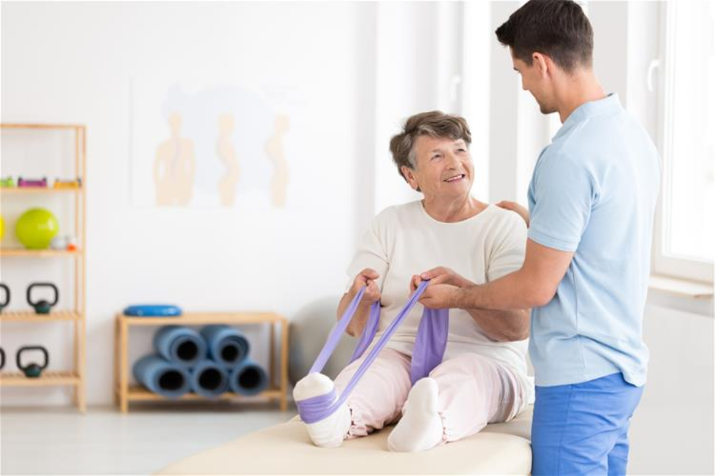 Stock photo of an older adult doing a leg stretch in a physiotherpy office with a physiotherapist