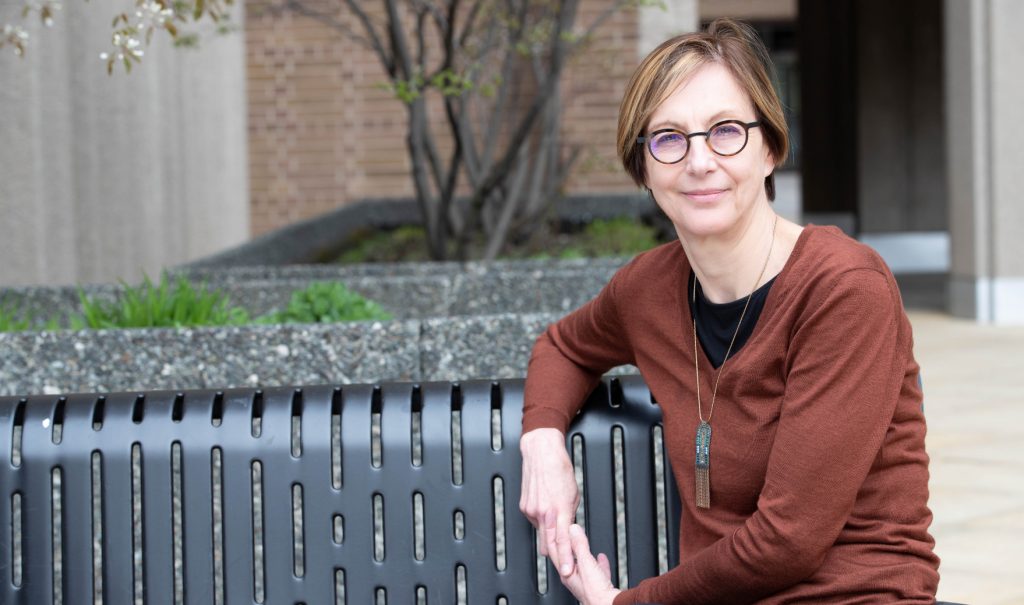 Judy Fudge is sitting on a bench outdoors on campus