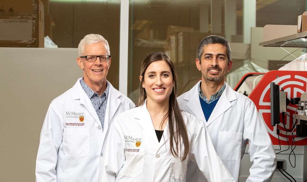 three researchers in lab coats smile in a lab.