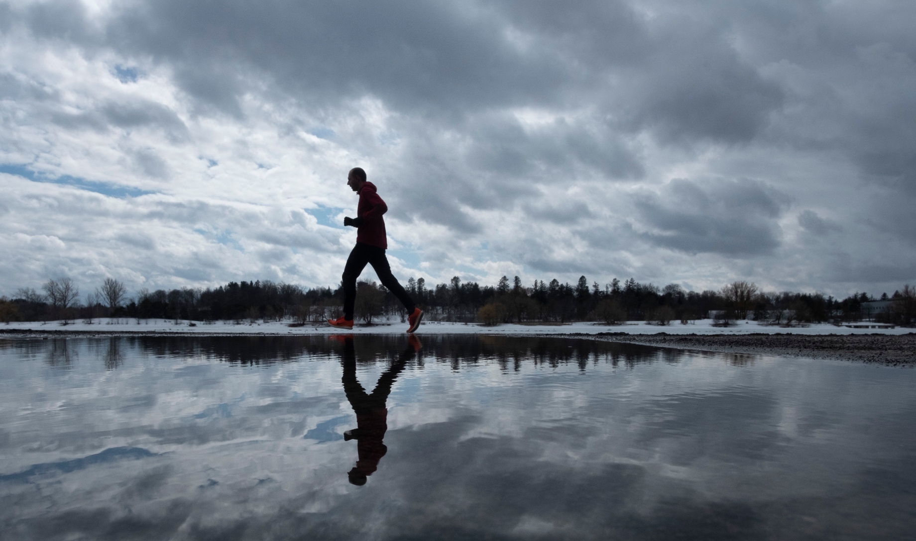 A jogger running solo past a big puddle that reflects them