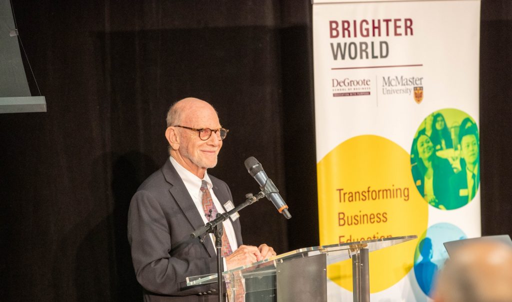 Len Waverman speaking at a podium with a McMaster banner behind him.