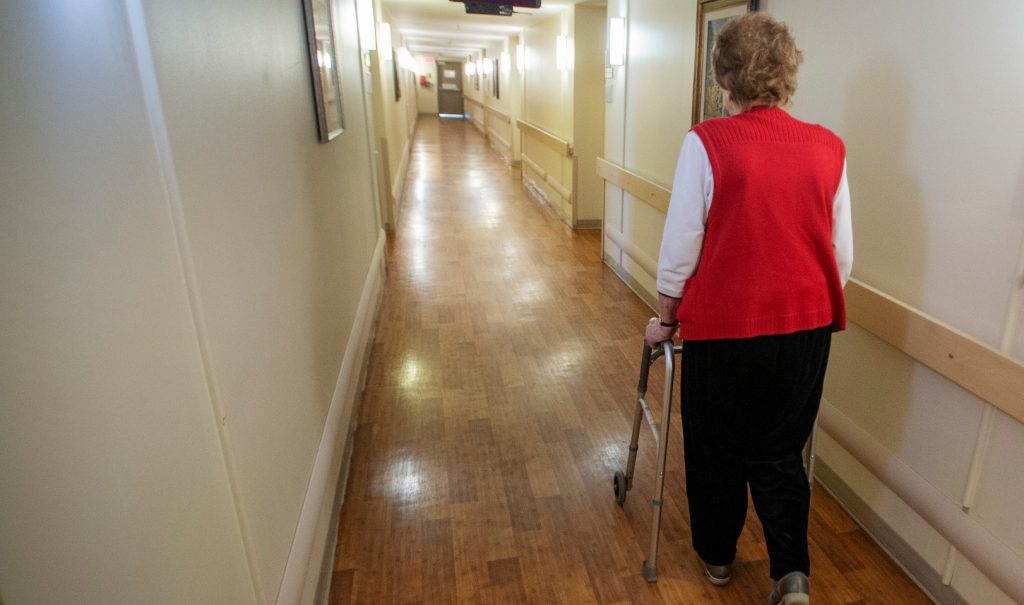 An older woman is using a walker to move down a long hallway
