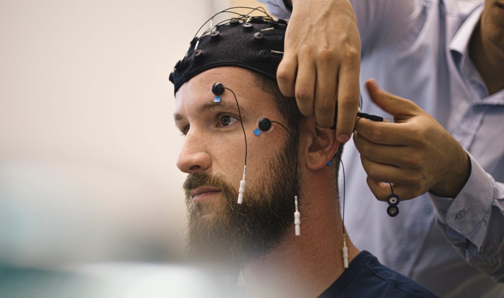 Closeup of a young, bearded man having electrodes hooked up to his head.