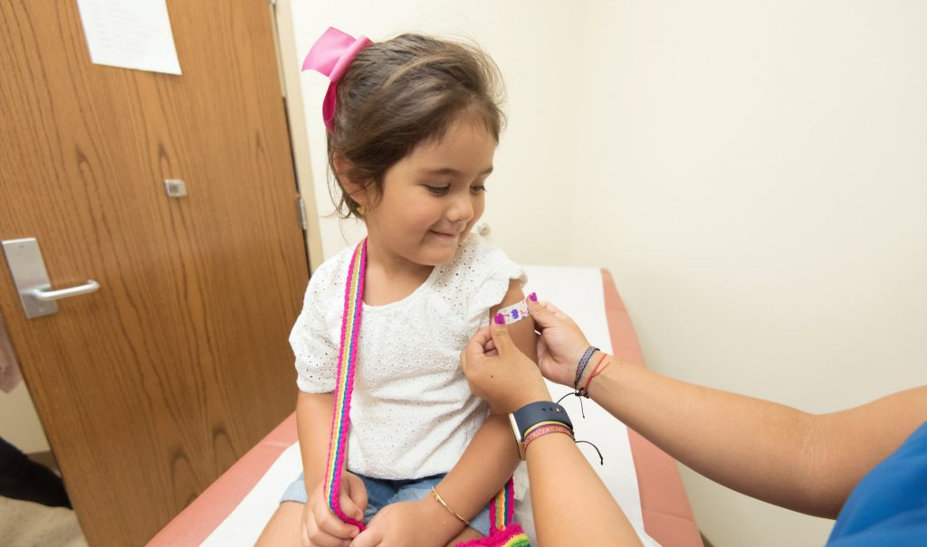 A little girl getting a colourful bandaid after a vaccination.