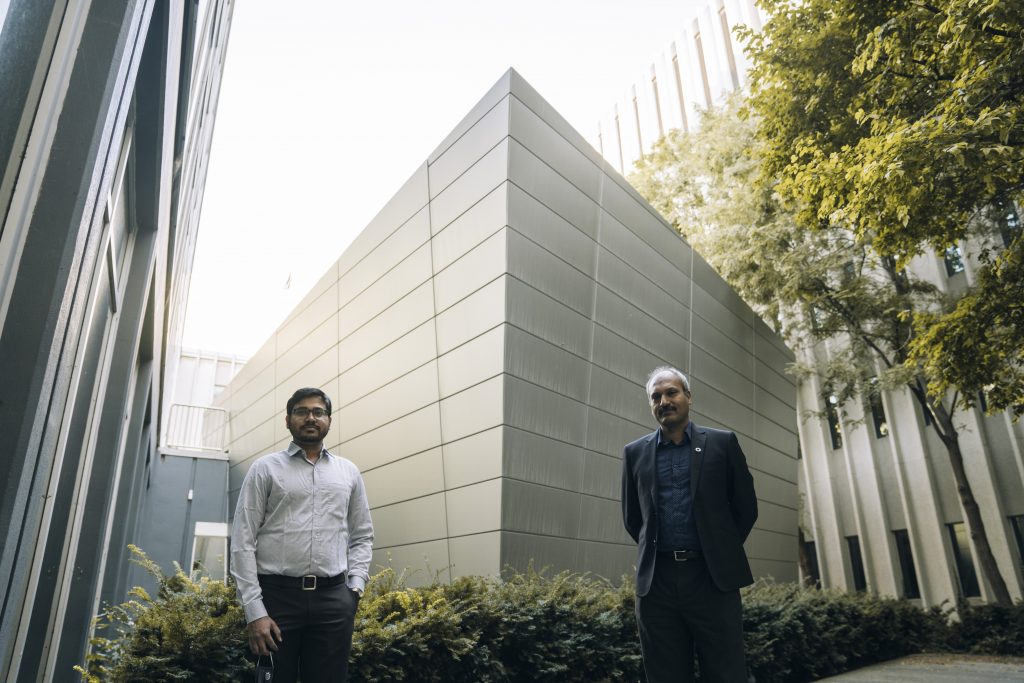 Smiling Rakesh Sahu and Ravi Selvaganapathy flank a building. They're standing six feet apart.