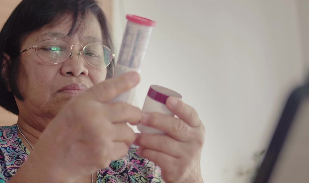 A woman with glasses or reading glasses is holding up 2 containers of medication and looking at the labels.